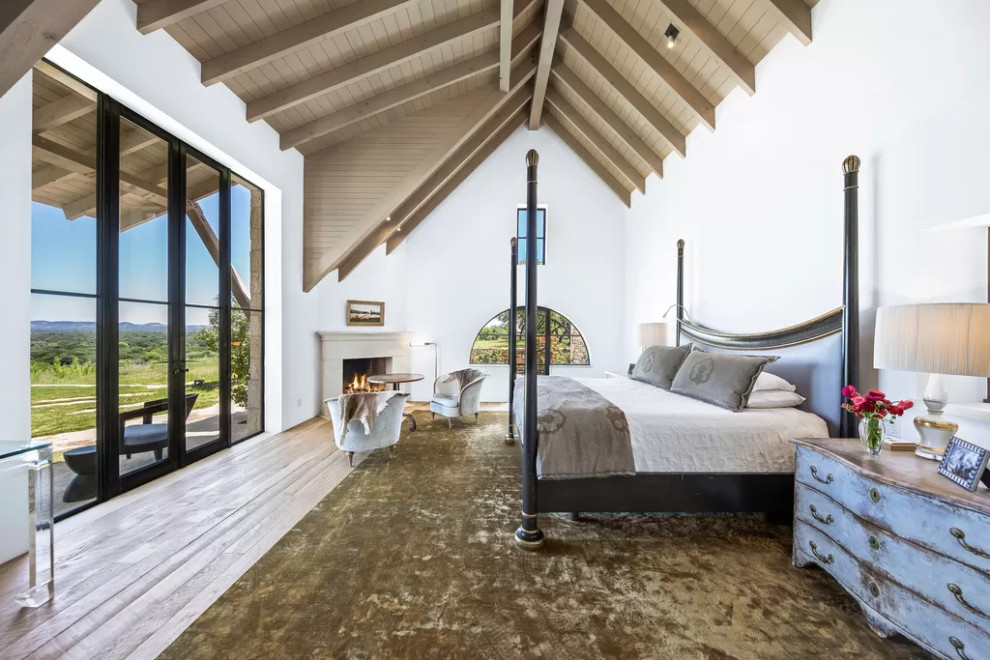 Großes Rustikales Hauptschlafzimmer mit weißer Wandfarbe, braunem Holzboden, Eckkamin, Kaminumrandung aus Beton, braunem Boden und gewölbter Decke in Austin