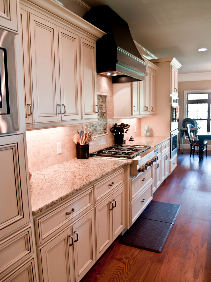 Design ideas for a mid-sized traditional l-shaped eat-in kitchen in Nashville with an undermount sink, flat-panel cabinets, white cabinets, granite benchtops, stone tile splashback, stainless steel appliances, medium hardwood floors and multiple islands.