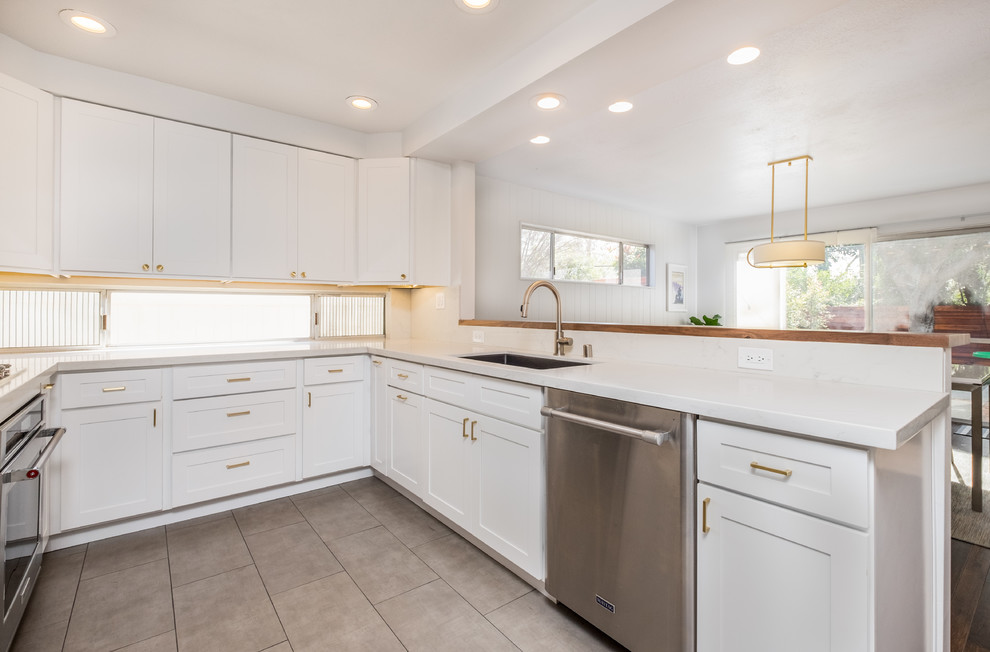Mid-sized midcentury u-shaped separate kitchen in Orange County with a drop-in sink, shaker cabinets, white cabinets, quartz benchtops, multi-coloured splashback, mosaic tile splashback, stainless steel appliances, porcelain floors and no island.