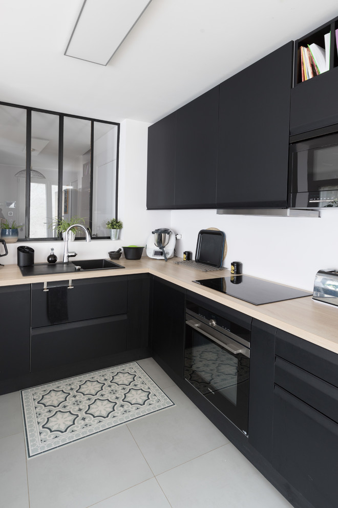 This is an example of a scandinavian l-shaped kitchen in Paris with a drop-in sink, flat-panel cabinets, black cabinets, white splashback, black appliances, grey floor and beige benchtop.