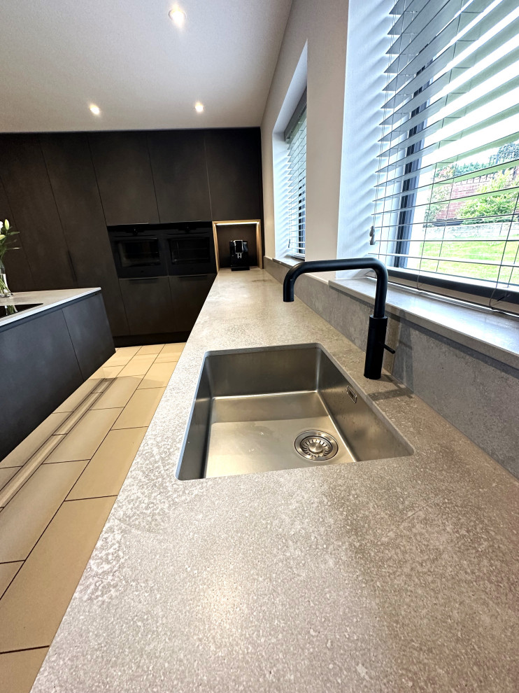 Mittelgroße Moderne Wohnküche in L-Form mit integriertem Waschbecken, flächenbündigen Schrankfronten, schwarzen Elektrogeräten, Porzellan-Bodenfliesen und Kücheninsel in Sonstige