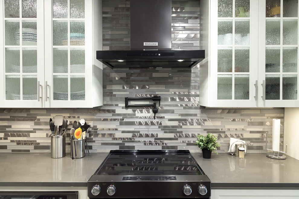Inspiration for a mid-sized transitional l-shaped porcelain tile and gray floor open concept kitchen remodel in Phoenix with an undermount sink, shaker cabinets, white cabinets, quartz countertops, gray backsplash, glass tile backsplash, black appliances, an island and gray countertops