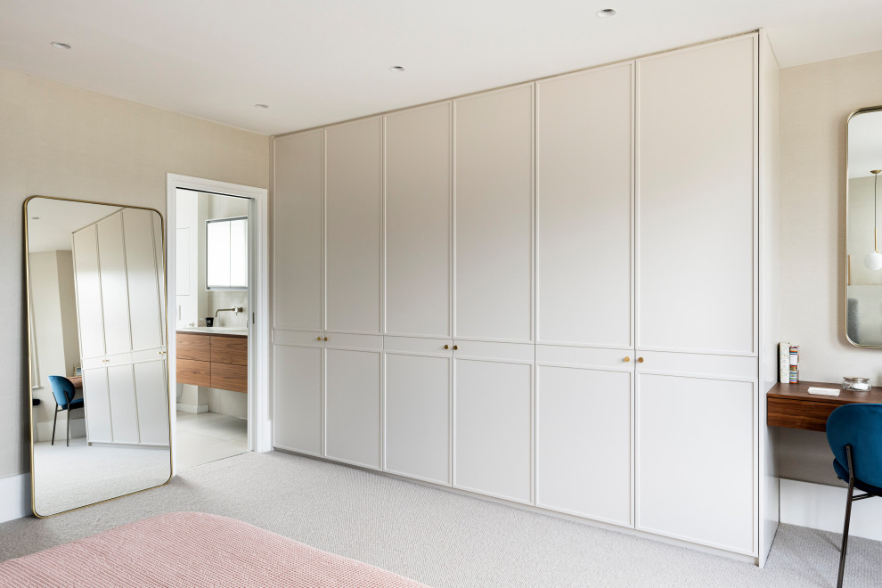 This is an example of a mid-sized contemporary gender-neutral storage and wardrobe in London with beaded inset cabinets, beige cabinets, carpet and beige floor.