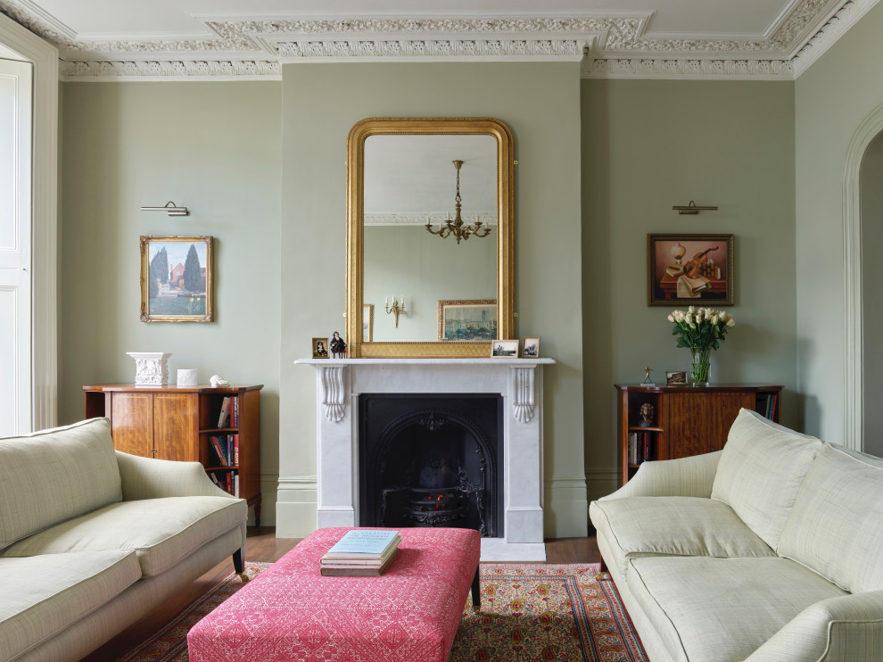 Cette image montre un grand salon victorien ouvert avec un mur vert, parquet foncé, une cheminée standard, un manteau de cheminée en pierre et un sol marron.