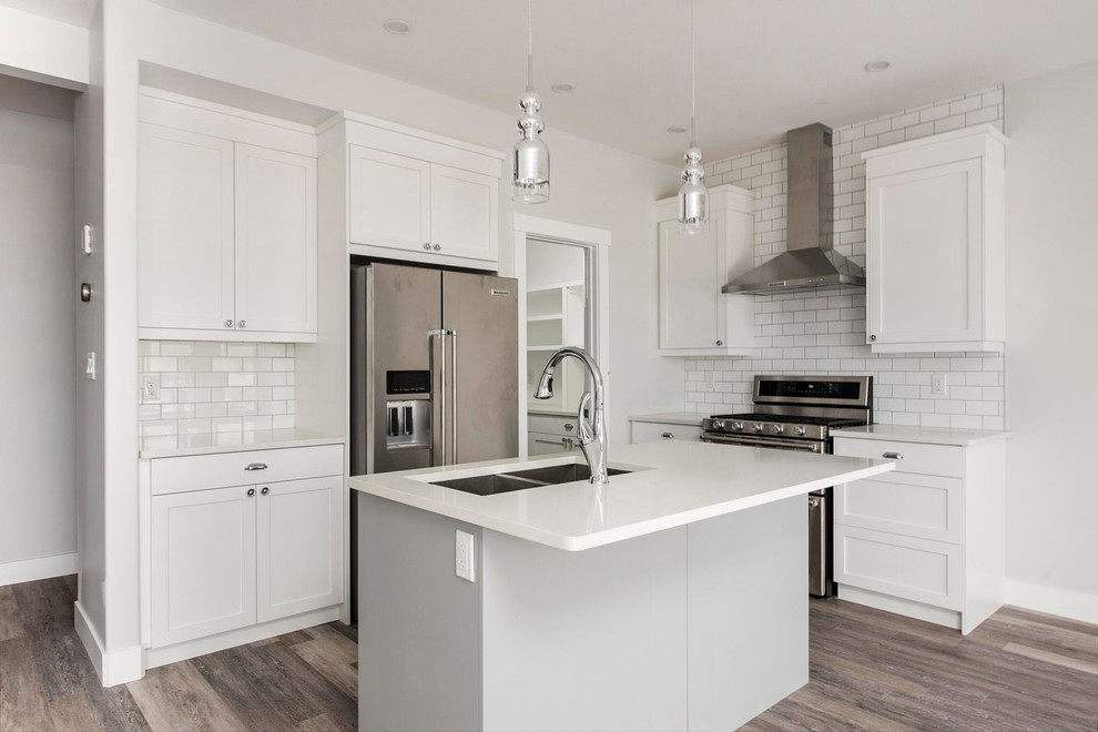 Example of a mid-sized transitional l-shaped medium tone wood floor and brown floor open concept kitchen design in Calgary with an undermount sink, shaker cabinets, white cabinets, quartzite countertops, white backsplash, subway tile backsplash, stainless steel appliances, an island and white countertops