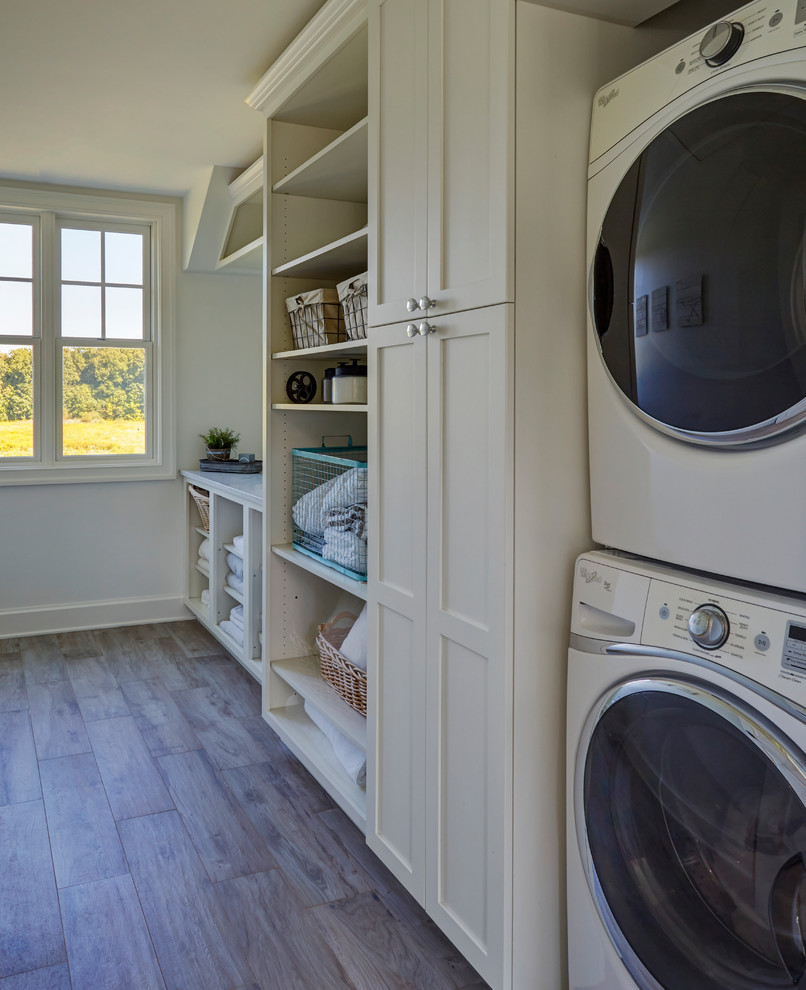 Large country u-shaped dedicated laundry room in Chicago with shaker cabinets, white cabinets, quartz benchtops, white walls, porcelain floors, a stacked washer and dryer, brown floor and grey benchtop.