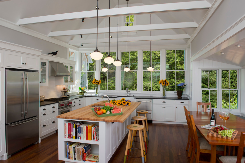 This is an example of a country l-shaped eat-in kitchen in Seattle with an undermount sink, shaker cabinets, white cabinets, wood benchtops, white splashback and stainless steel appliances.