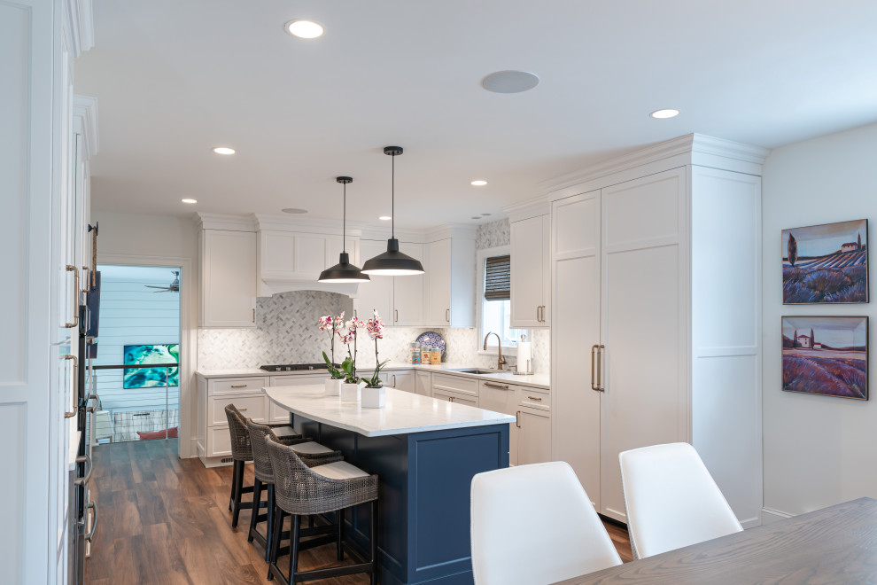 This is an example of a large beach style u-shaped eat-in kitchen in Philadelphia with an undermount sink, shaker cabinets, white cabinets, quartz benchtops, white splashback, marble splashback, panelled appliances, vinyl floors, with island, brown floor and white benchtop.