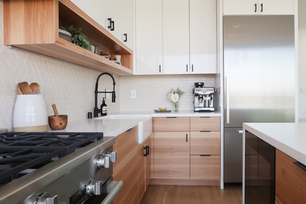 Design ideas for a medium sized contemporary l-shaped kitchen/diner in San Francisco with a belfast sink, flat-panel cabinets, white cabinets, engineered stone countertops, ceramic splashback, stainless steel appliances, light hardwood flooring, an island and beige floors.