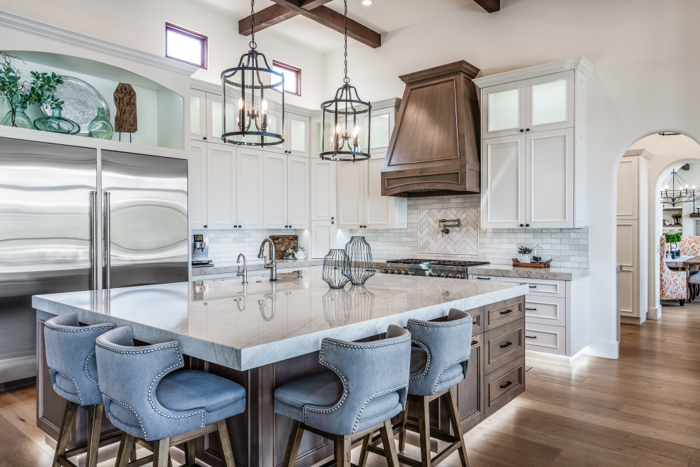 Inspiration for a transitional l-shaped medium tone wood floor, brown floor and exposed beam kitchen remodel in Phoenix with a farmhouse sink, recessed-panel cabinets, white cabinets, white backsplash, stainless steel appliances, an island and gray countertops