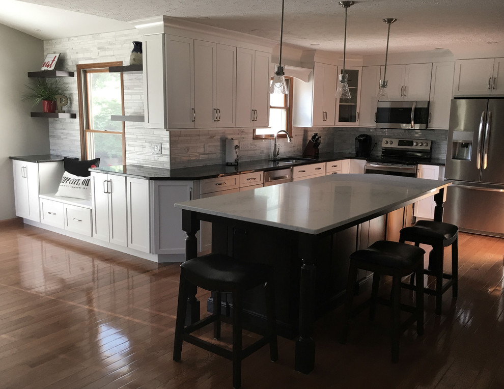 Inspiration for a large transitional single-wall medium tone wood floor eat-in kitchen remodel with an undermount sink, shaker cabinets, white cabinets, granite countertops, multicolored backsplash, marble backsplash, stainless steel appliances, an island and black countertops