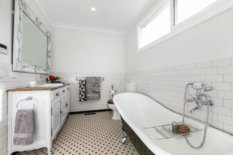 Design ideas for a traditional master bathroom in Melbourne with an integrated sink, furniture-like cabinets, distressed cabinets, wood benchtops, a claw-foot tub, a two-piece toilet, multi-coloured tile, porcelain tile, white walls and mosaic tile floors.