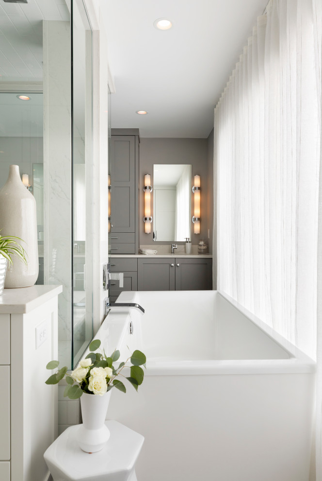 Photo of a large transitional master bathroom in Minneapolis with shaker cabinets, grey cabinets, a freestanding tub, an open shower, a one-piece toilet, grey walls, porcelain floors, an undermount sink, solid surface benchtops, grey floor, a hinged shower door, white benchtops, a shower seat, a double vanity and a built-in vanity.