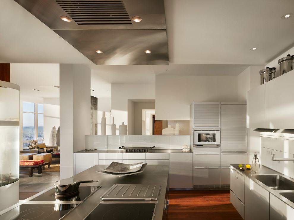 Design ideas for an expansive contemporary u-shaped open plan kitchen in Philadelphia with a double-bowl sink, flat-panel cabinets, white cabinets, white splashback, glass sheet splashback, medium hardwood floors and with island.