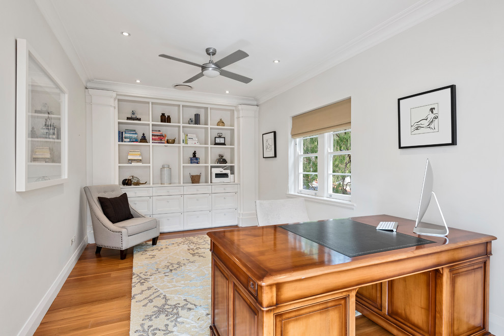 This is an example of a mid-sized traditional study room in Sydney with white walls, medium hardwood floors, no fireplace, a freestanding desk and brown floor.