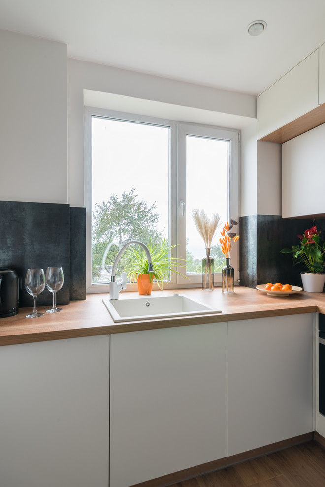 This is an example of a small contemporary l-shaped separate kitchen in Moscow with a drop-in sink, flat-panel cabinets, white cabinets, black splashback, no island, brown floor and brown benchtop.