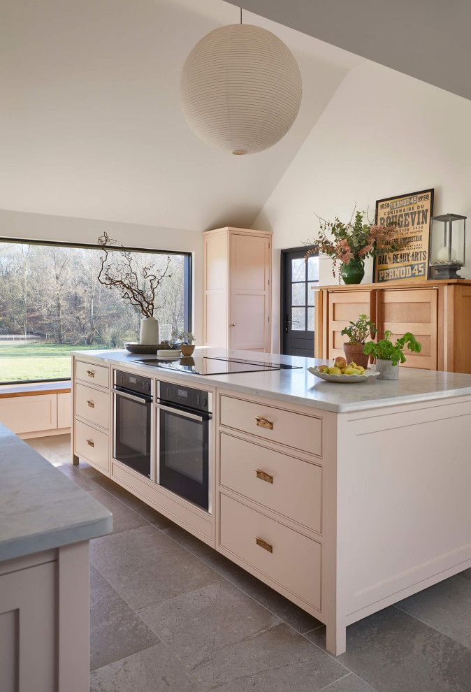 Large country single-wall open plan kitchen in London with a farmhouse sink, shaker cabinets, pink cabinets, quartzite benchtops, pink splashback, black appliances, ceramic floors, with island, multi-coloured floor, grey benchtop and vaulted.