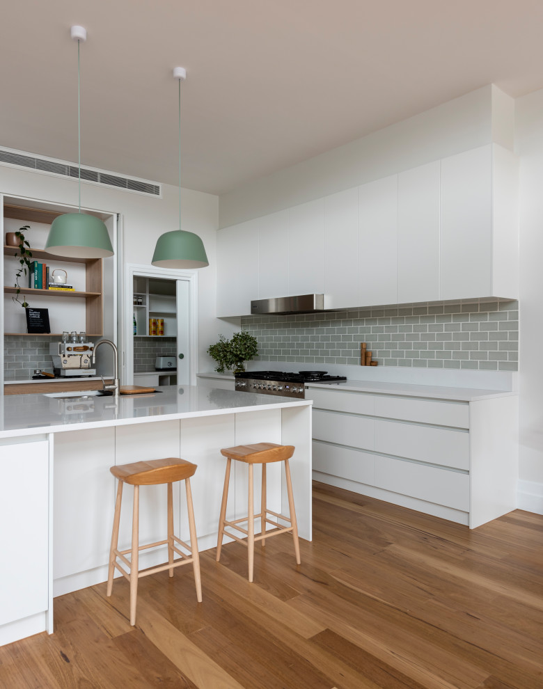Inspiration for a large contemporary l-shaped eat-in kitchen in Melbourne with a double-bowl sink, flat-panel cabinets, white cabinets, quartz benchtops, green splashback, subway tile splashback, stainless steel appliances, medium hardwood floors, with island, brown floor and white benchtop.