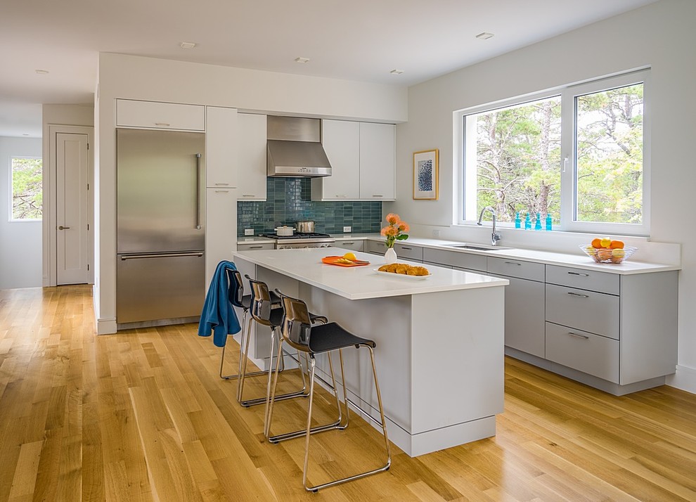 Mid-sized minimalist l-shaped light wood floor open concept kitchen photo in Boston with an undermount sink, flat-panel cabinets, gray cabinets, quartz countertops, white backsplash, stainless steel appliances and an island