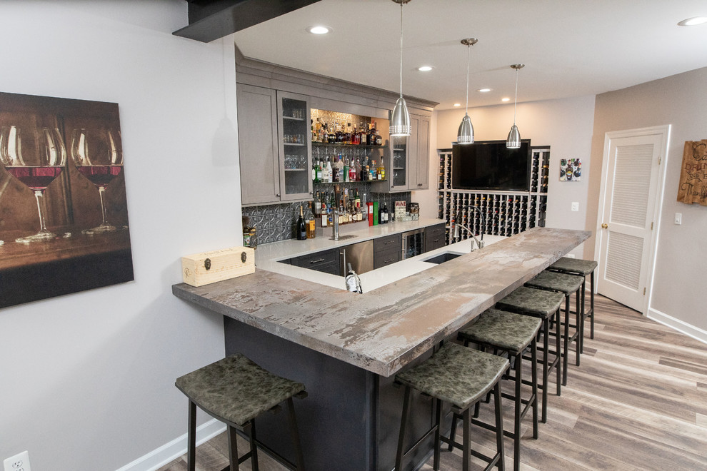 Photo of a small industrial u-shaped seated home bar in DC Metro with an undermount sink, shaker cabinets, medium wood cabinets, quartz benchtops, grey splashback, metal splashback, vinyl floors, brown floor and grey benchtop.