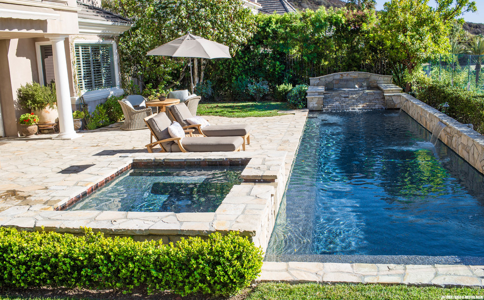 Large transitional backyard rectangular lap pool in Los Angeles with a water feature and natural stone pavers.