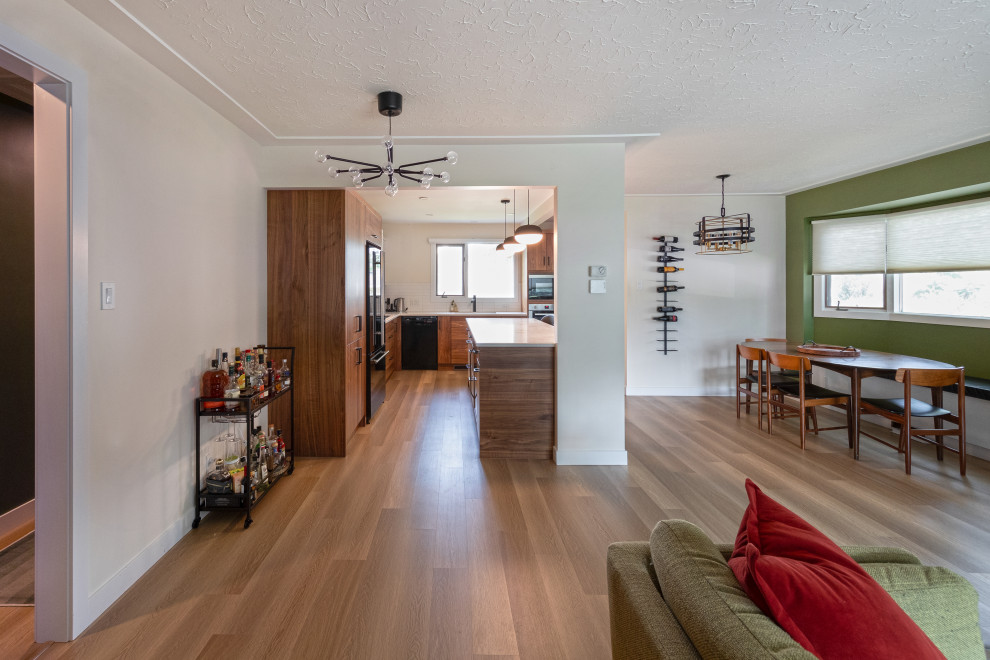 This is an example of a mid-sized midcentury u-shaped open plan kitchen in Edmonton with a double-bowl sink, flat-panel cabinets, medium wood cabinets, quartz benchtops, white splashback, ceramic splashback, stainless steel appliances, vinyl floors, with island, brown floor and white benchtop.