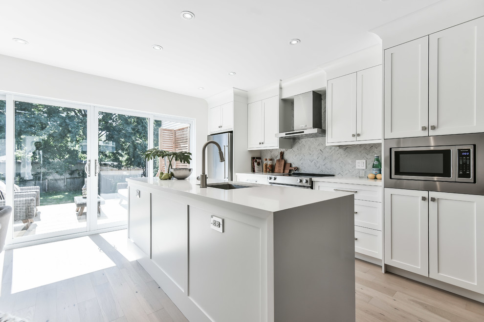 Inspiration for a transitional galley light wood floor and beige floor kitchen remodel with an undermount sink, shaker cabinets, white cabinets, white backsplash, marble backsplash, stainless steel appliances, an island and white countertops