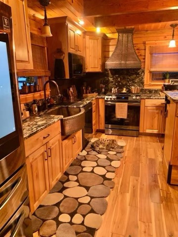 他の地域にある高級な中くらいなラスティックスタイルのおしゃれなキッチン (エプロンフロントシンク、レイズドパネル扉のキャビネット、中間色木目調キャビネット、御影石カウンター、茶色いキッチンパネル、石スラブのキッチンパネル、シルバーの調理設備、クッションフロア、ベージュの床、茶色いキッチンカウンター) の写真