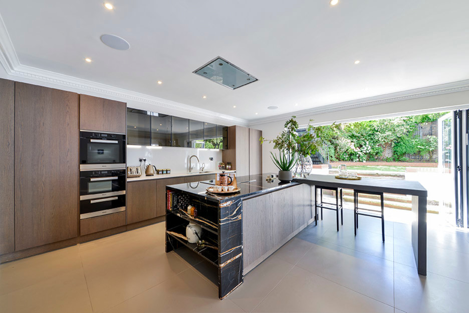 Photo of an expansive contemporary l-shaped eat-in kitchen in London with an undermount sink, medium wood cabinets, marble benchtops, white splashback, panelled appliances, with island and flat-panel cabinets.