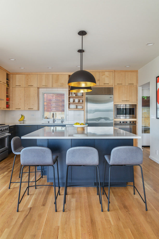 Photo of a large contemporary l-shaped open plan kitchen in Seattle with an undermount sink, flat-panel cabinets, light wood cabinets, quartz benchtops, white splashback, ceramic splashback, stainless steel appliances, light hardwood floors, with island, white benchtop and brown floor.