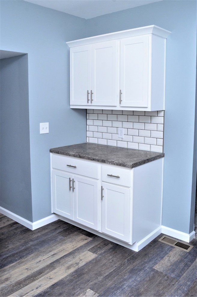 Photo of a mid-sized transitional u-shaped separate kitchen in Other with a drop-in sink, shaker cabinets, white cabinets, laminate benchtops, white splashback, subway tile splashback, stainless steel appliances, light hardwood floors, no island, grey floor and grey benchtop.