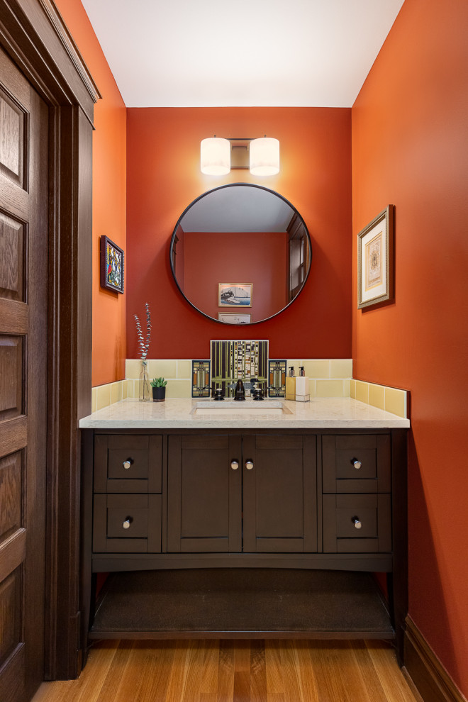 Exemple d'un petit WC et toilettes craftsman avec un placard à porte shaker, des portes de placard marrons, un mur orange, parquet clair, meuble-lavabo encastré et un lavabo encastré.