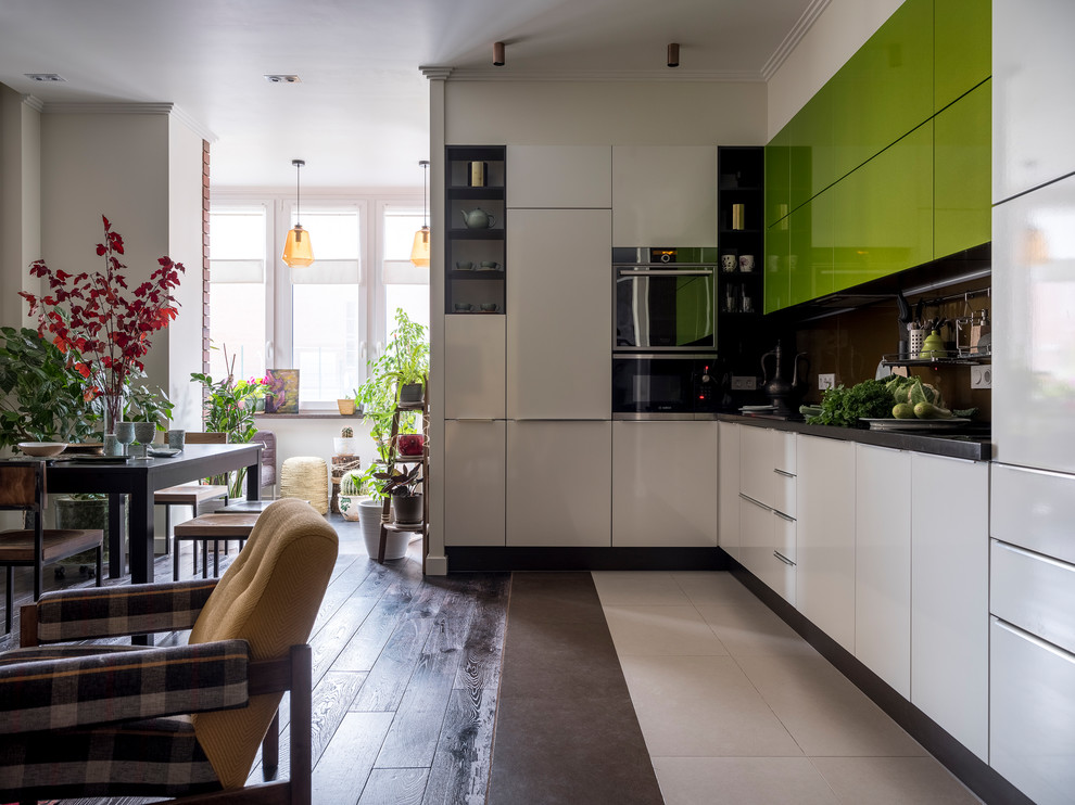 Mid-sized eclectic single-wall open plan kitchen in Moscow with a double-bowl sink, flat-panel cabinets, green cabinets, brown splashback, glass sheet splashback, stainless steel appliances, dark hardwood floors, brown floor and black benchtop.