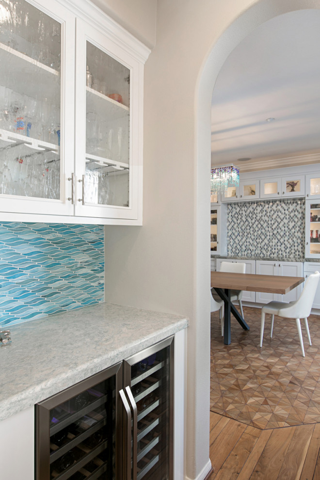 Photo of a mid-sized contemporary l-shaped home bar in San Diego with an undermount sink, beaded inset cabinets, white cabinets, quartzite benchtops, blue splashback, glass tile splashback, light hardwood floors, beige floor and white benchtop.
