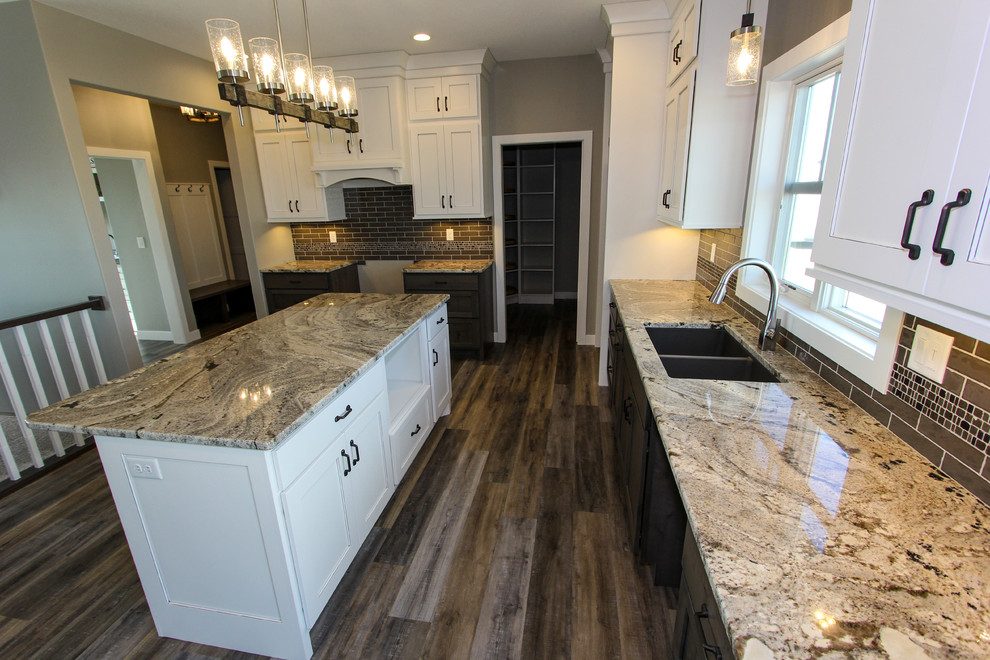 Inspiration for a mid-sized transitional l-shaped laminate floor and brown floor eat-in kitchen remodel in Minneapolis with an undermount sink, shaker cabinets, white cabinets, granite countertops, gray backsplash, ceramic backsplash, an island and multicolored countertops