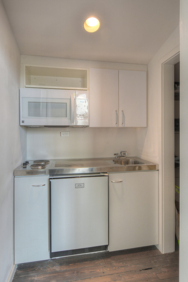 This is an example of a small modern single-wall separate kitchen in Other with a drop-in sink, flat-panel cabinets, white cabinets, white appliances and dark hardwood floors.