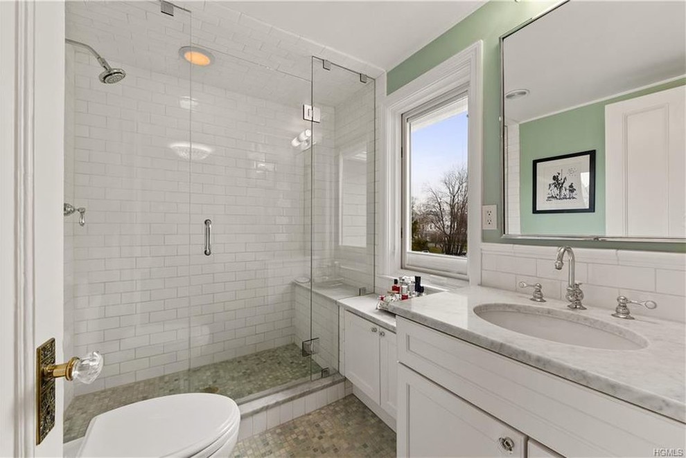 Design ideas for a mid-sized transitional 3/4 bathroom in New York with recessed-panel cabinets, white cabinets, an alcove shower, white tile, subway tile, an undermount sink, marble benchtops, brown floor, a hinged shower door, grey benchtops, a two-piece toilet, green walls and mosaic tile floors.