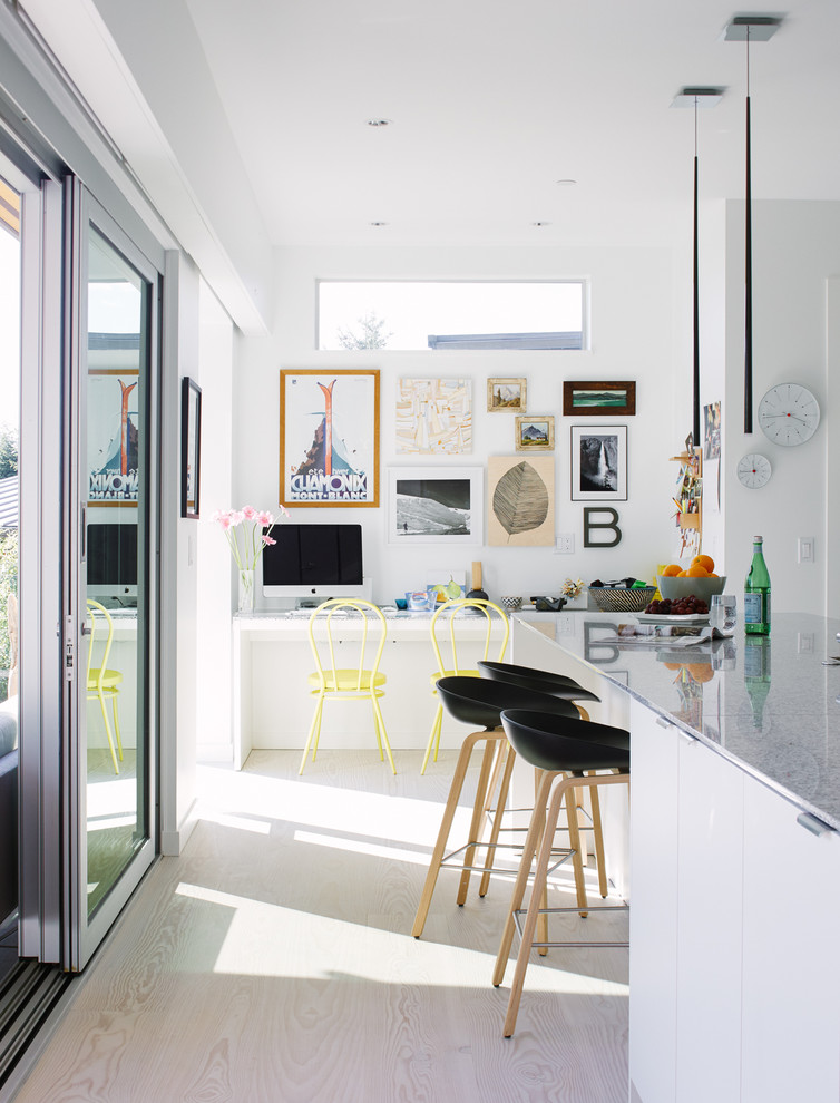 Inspiration for a mid-sized eclectic open plan kitchen in Vancouver with flat-panel cabinets, white cabinets, grey splashback, light hardwood floors and a peninsula.