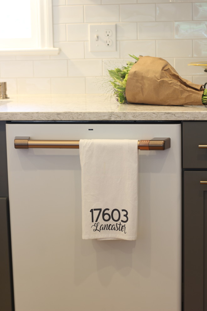 Example of a mid-sized transitional u-shaped medium tone wood floor and brown floor enclosed kitchen design with a farmhouse sink, shaker cabinets, white cabinets, quartz countertops, white backsplash, subway tile backsplash, white appliances, no island and beige countertops