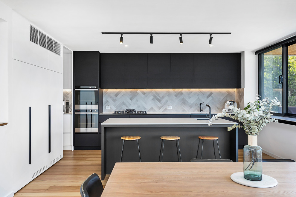 This is an example of a large contemporary l-shaped eat-in kitchen in Wollongong with an undermount sink, flat-panel cabinets, black cabinets, grey splashback, panelled appliances, with island, beige floor and white benchtop.