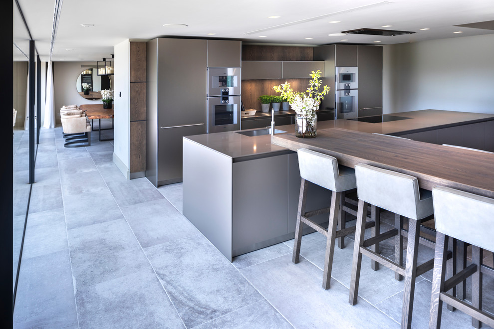 This is an example of a large contemporary open plan kitchen in Cheshire with an integrated sink, flat-panel cabinets, medium wood cabinets, stainless steel benchtops, timber splashback, stainless steel appliances, ceramic floors, multiple islands, white floor and green benchtop.