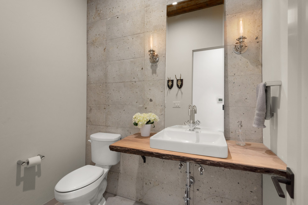 На фото: туалет среднего размера в стиле неоклассика (современная классика) с унитазом-моноблоком, серой плиткой, каменной плиткой, серыми стенами, бетонным полом, настольной раковиной, столешницей из дерева, серым полом и подвесной тумбой