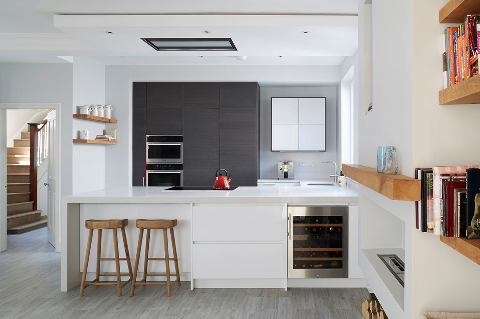 Design ideas for a mid-sized contemporary u-shaped open plan kitchen in London with flat-panel cabinets, dark wood cabinets, a peninsula, an undermount sink, stainless steel appliances, solid surface benchtops and light hardwood floors.