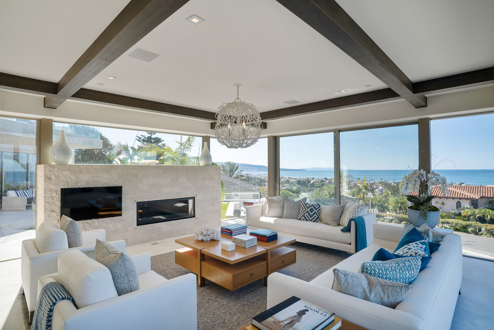 This is an example of a large beach style open concept living room in Los Angeles with white walls, limestone floors, a stone fireplace surround, a ribbon fireplace and a wall-mounted tv.