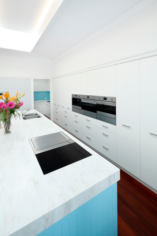 Inspiration for a large traditional single-wall open plan kitchen in Sydney with an undermount sink, flat-panel cabinets, white cabinets, quartz benchtops, blue splashback, glass sheet splashback, stainless steel appliances, medium hardwood floors, with island, red floor and white benchtop.