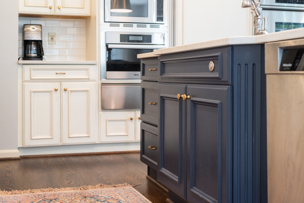 Transitional medium tone wood floor and brown floor kitchen photo in DC Metro with an undermount sink, recessed-panel cabinets, white cabinets, granite countertops, white backsplash, subway tile backsplash, stainless steel appliances, an island and white countertops