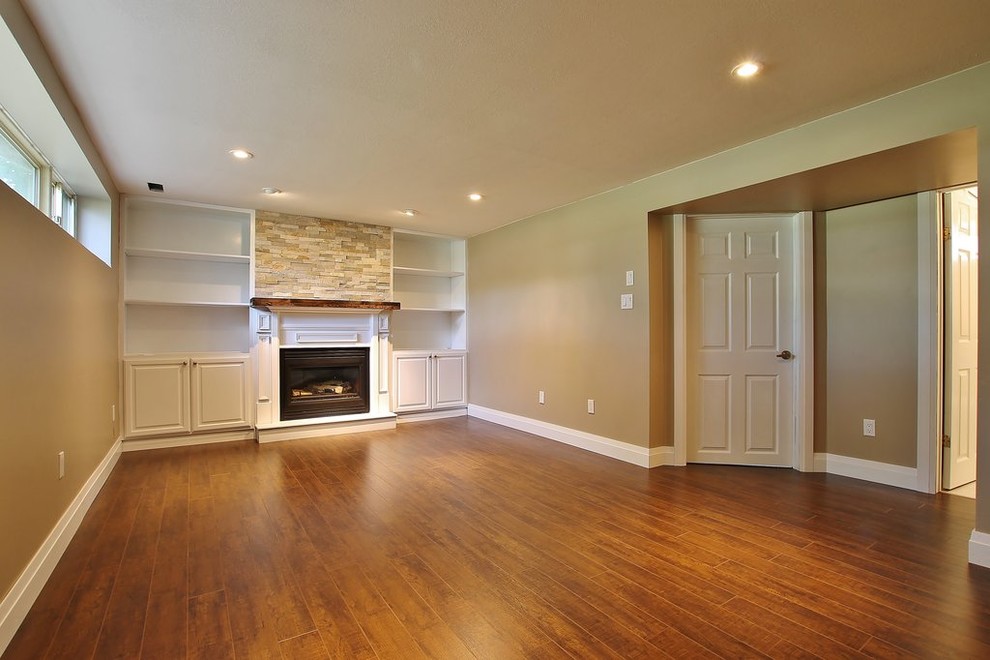 Photo of a mid-sized fully buried basement in Other with beige walls, medium hardwood floors, a standard fireplace and a stone fireplace surround.