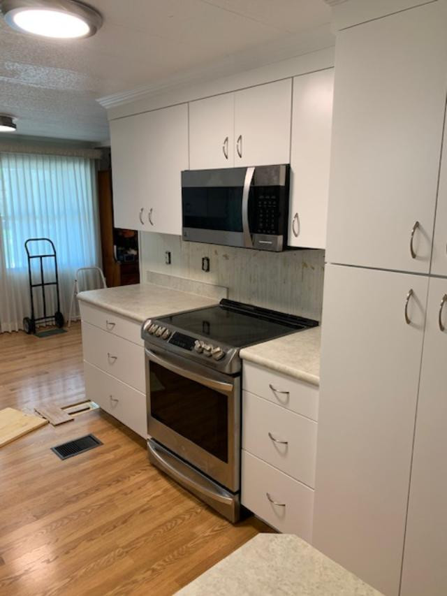 Example of a large u-shaped kitchen pantry design with a farmhouse sink, flat-panel cabinets, white cabinets, laminate countertops, white backsplash, stainless steel appliances, a peninsula and white countertops