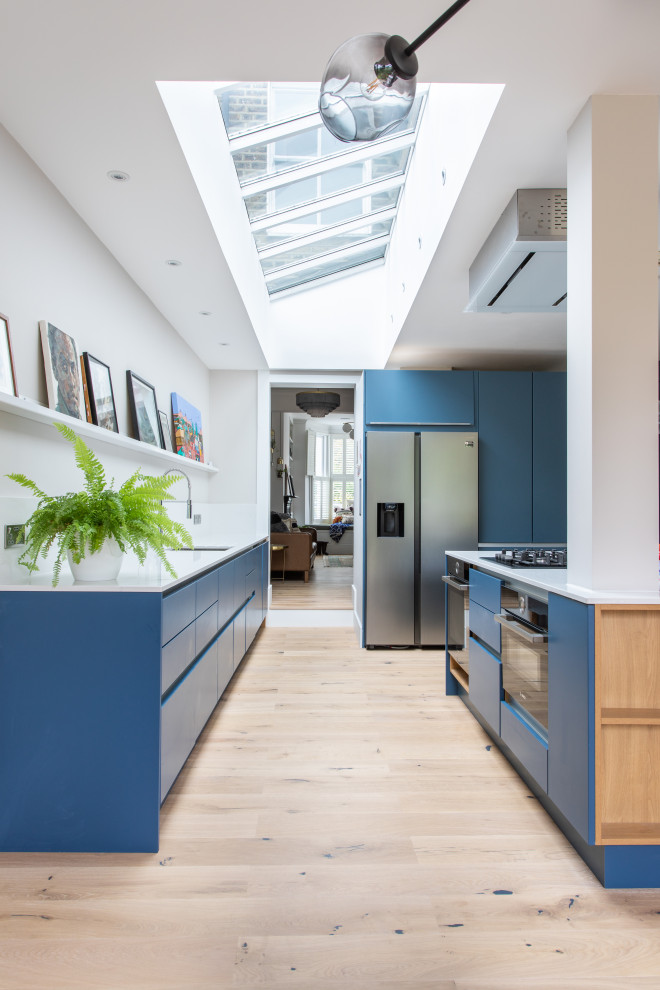 Design ideas for a large contemporary l-shaped eat-in kitchen in London with a single-bowl sink, flat-panel cabinets, blue cabinets, solid surface benchtops, white splashback, panelled appliances, light hardwood floors, with island and white benchtop.