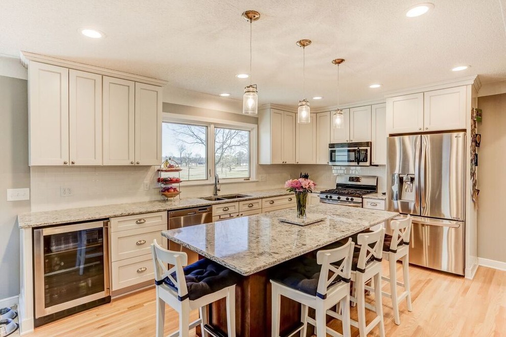 Photo of a large transitional l-shaped eat-in kitchen in Minneapolis with an undermount sink, recessed-panel cabinets, white cabinets, granite benchtops, white splashback, subway tile splashback, stainless steel appliances, light hardwood floors, with island, beige floor and grey benchtop.